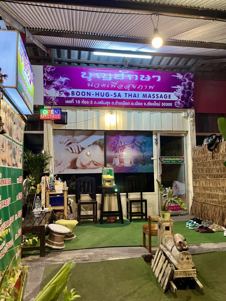 「Boon-Hug-Sa Thai Massage」店頭マッサージの写真が貼られ、椅子や靴が並んでいる