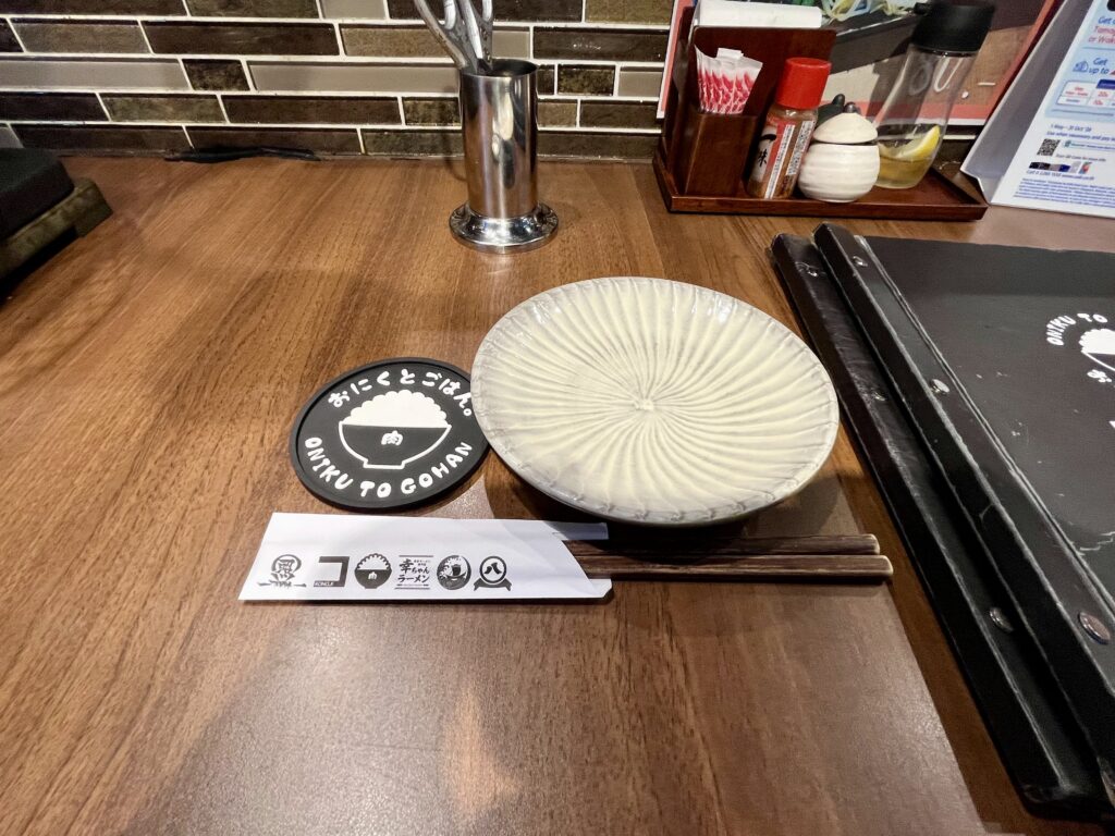 日本街(にほんまち/Nihonmachi)にあるおにくとごはん。のカウンター席、テーブルに箸とお皿、コースターが並ぶ