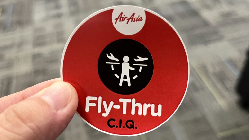 AirAsiaの「Fly-Thru C.I.Q.」と書かれた赤いステッカーを持っている