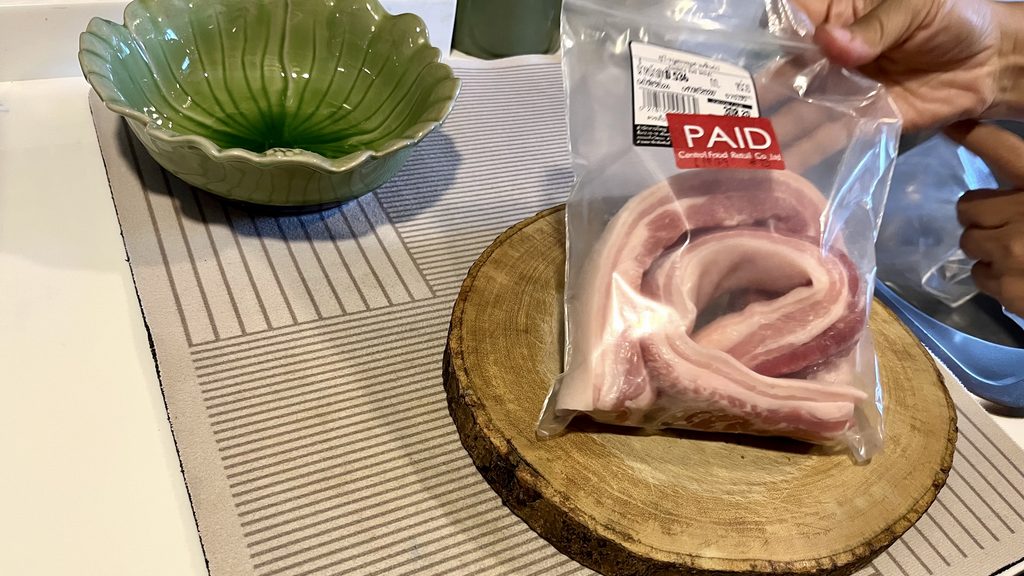 タイの家庭のキッチンのまな板に、豚肉が入ったビニール袋を置いているところ