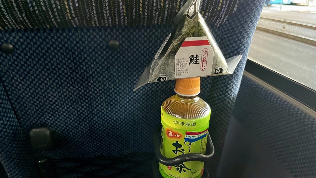 バス車内の飲み物ホルダーに、ペットボトルのお茶とおにぎりが重ねて置かれている