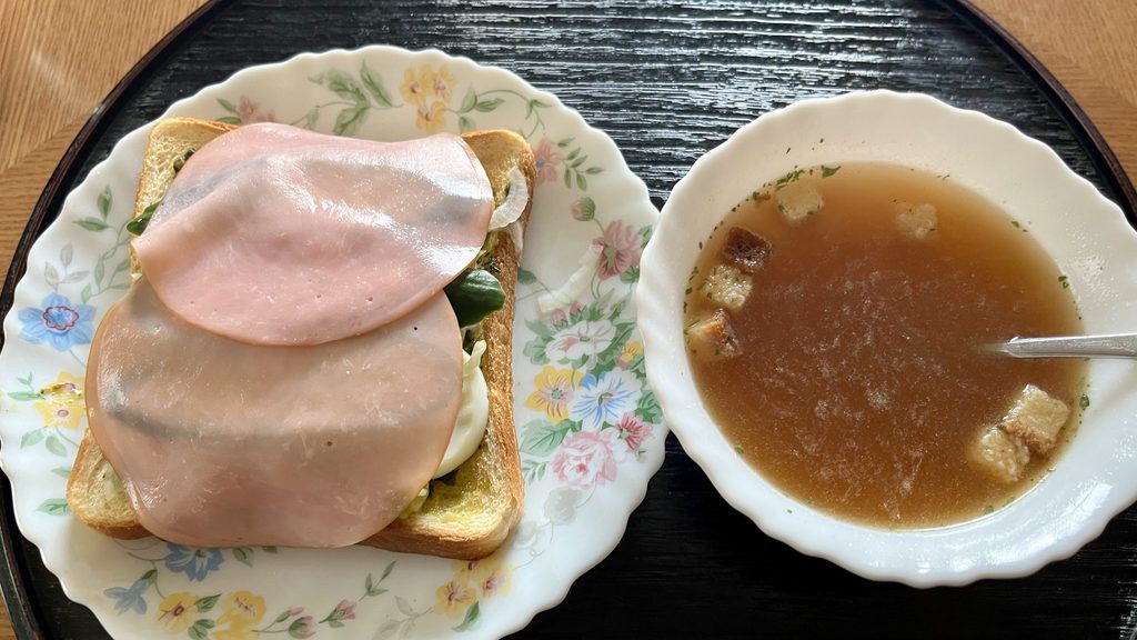 黒いお盆にオープンサンドイッチとコンソメスープが乗っている