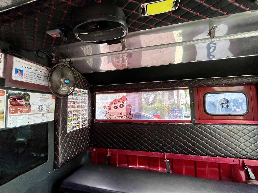 MuvMi(ムーブミー)の車内、赤いソンテウに黒の革張りでリノベーションしてある。窓にはアニメキャラクターが貼ってある